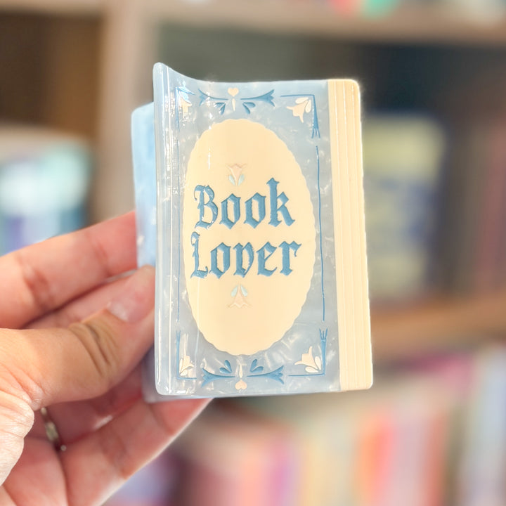 A hand holds a miniature book-shaped item labeled &