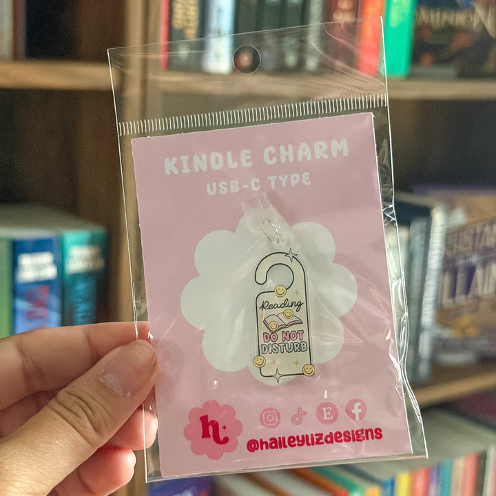 A hand holding a clear plastic bag containing a pink card with a white cloud-shaped cutout and a small hanging charm that says &