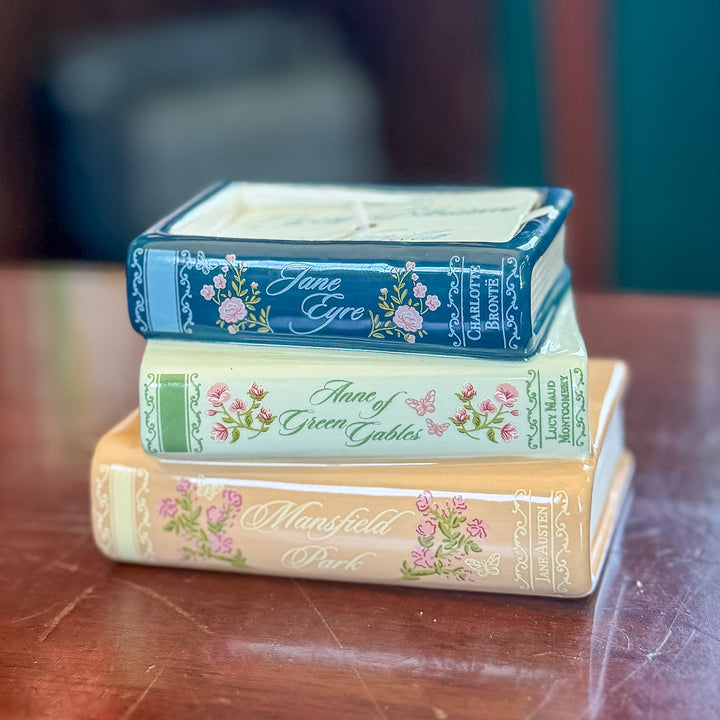 Three decorative book-shaped items stacked on a wooden surface, featuring floral designs and titles including Jane Eyre, Anne of Green Gables, and Mansfield Park.
