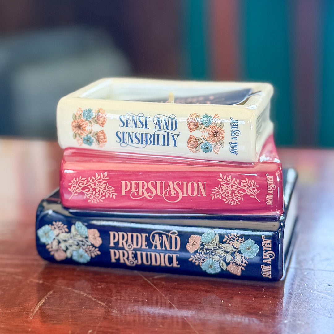 Three decorative books stacked on a wooden table, featuring the titles 'Pride and Prejudice', 'Persuasion', and 'Sense and Sensibility' with floral illustrations and the name Jane Austen on the spines.