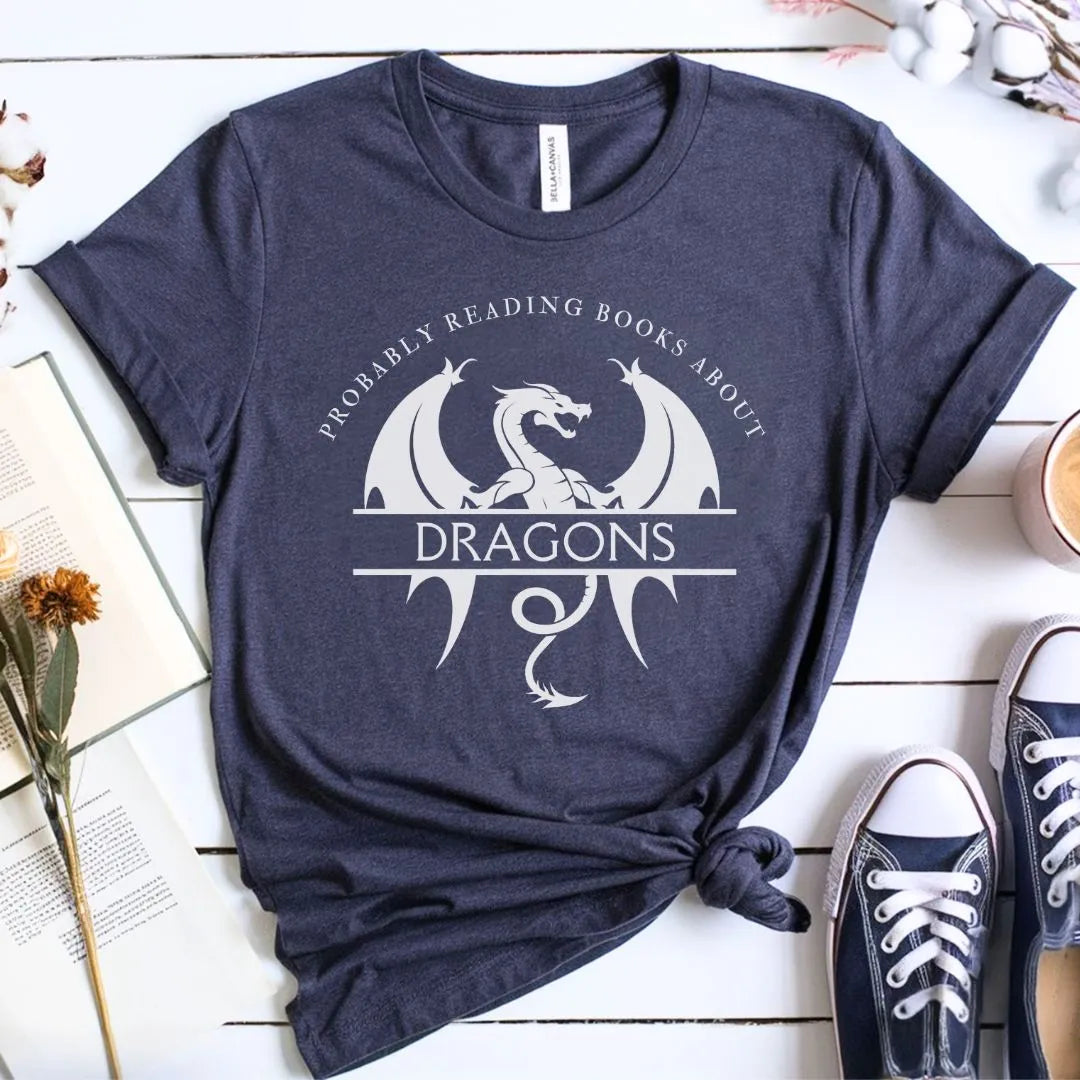 Navy blue t-shirt with dragon graphic and text on a wooden surface with books and shoes.
