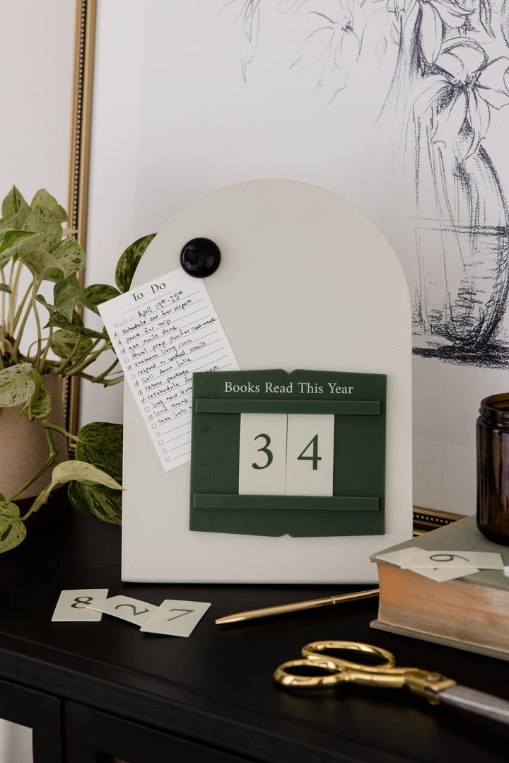 A white arched magnetic board with a dark green block calendar showing &