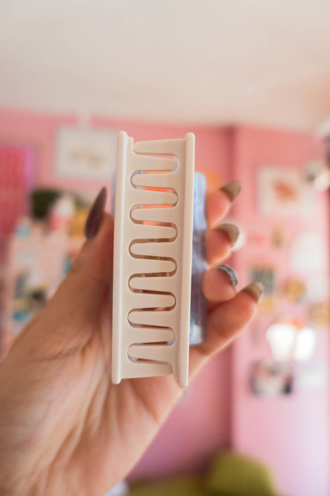 Hand holding a white hair dryer diffuser with a blurred pink room background