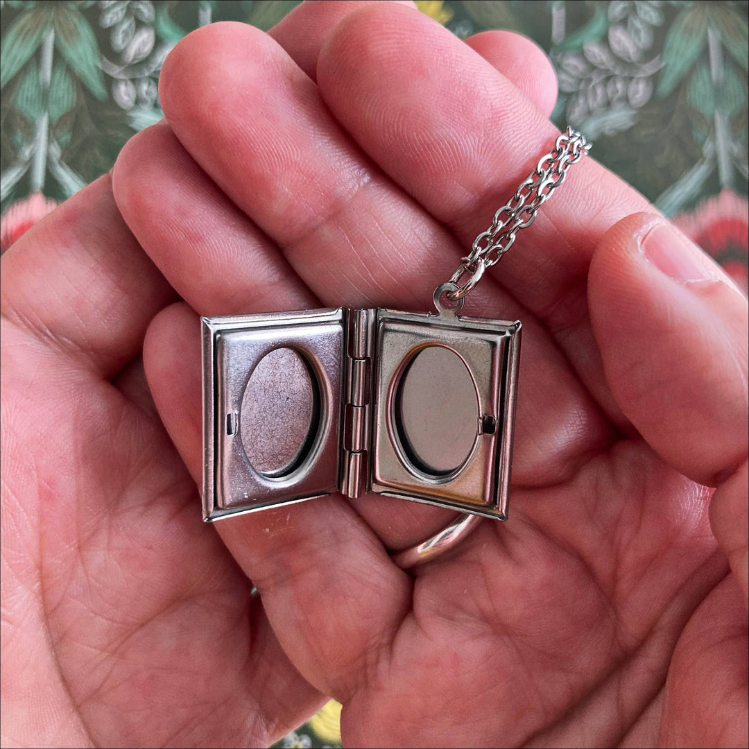 Silver locket with chain held in a hand against a floral background