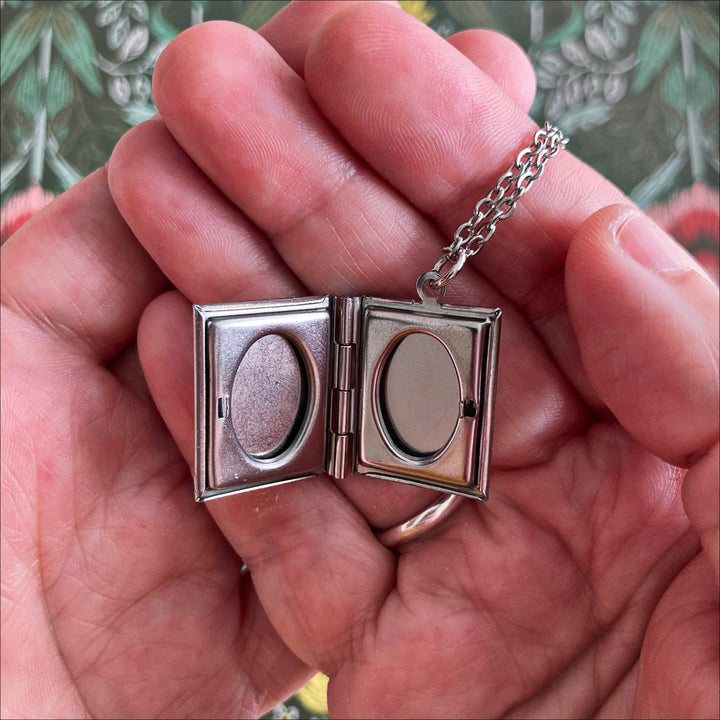 Silver locket with chain held in a hand against a floral background