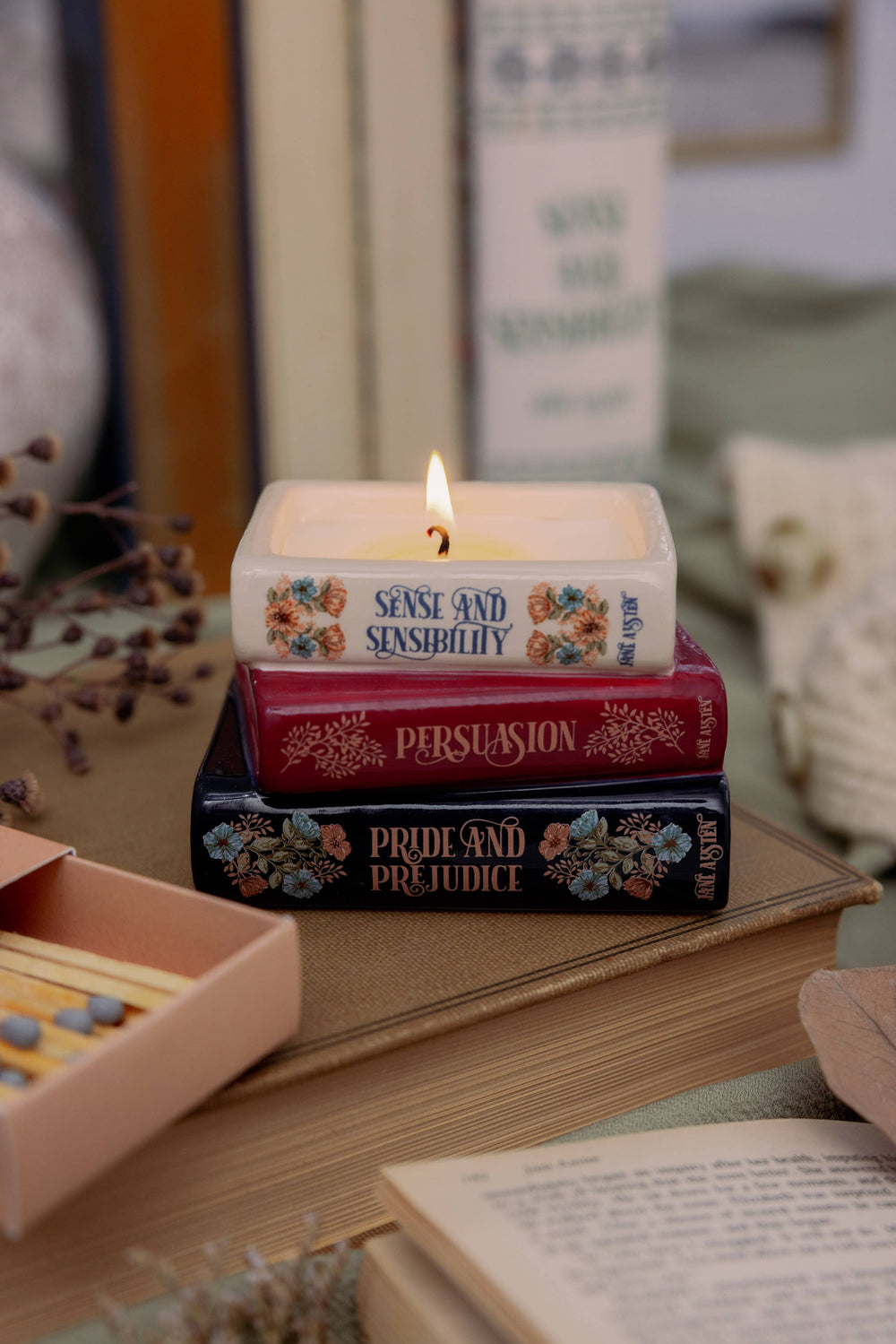 Lit Jane Austen bookstack candle with cream, burgundy, and navy floral book spines, displayed on a vintage book.