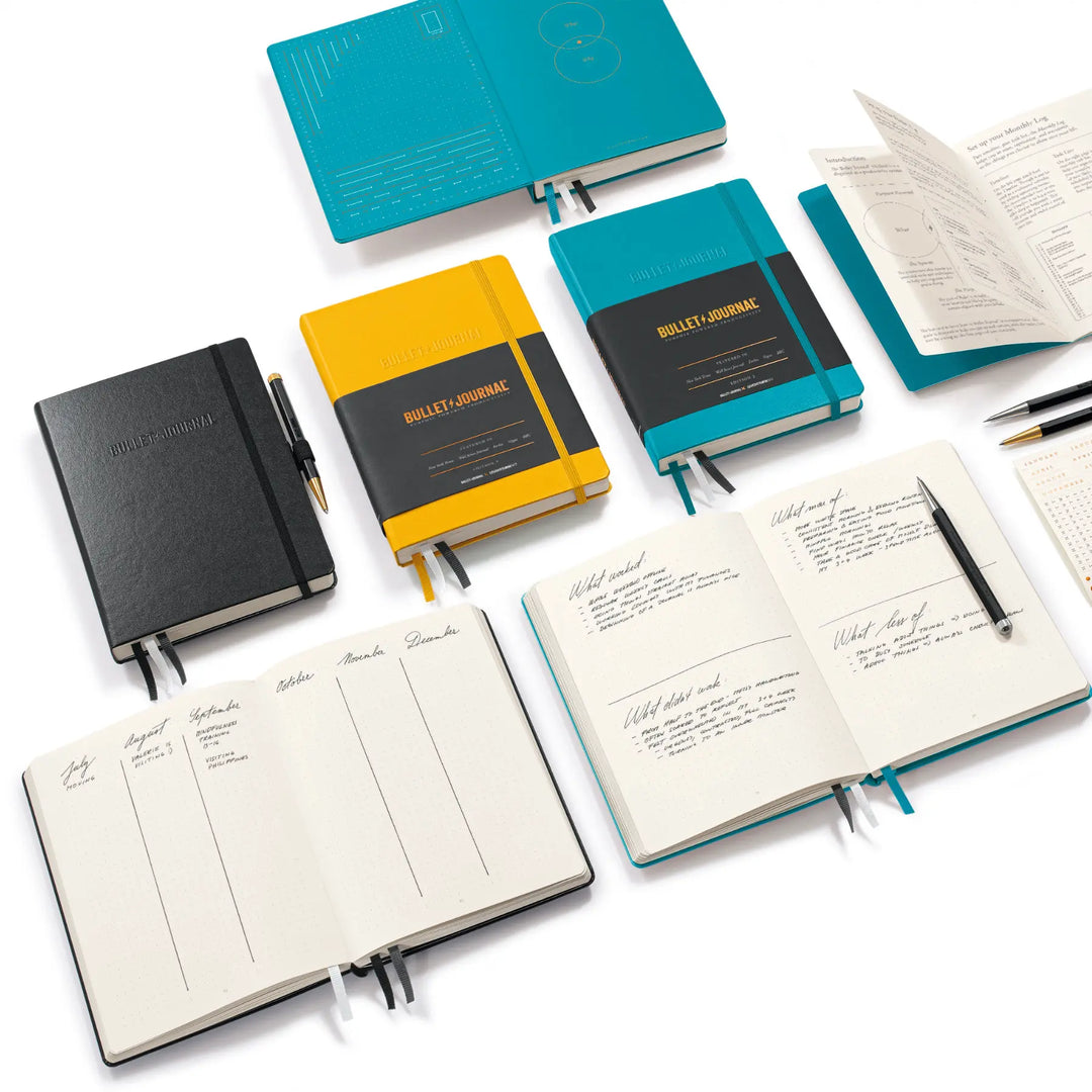 Collection of bullet journal notebooks in various colors with open pages on a white background.