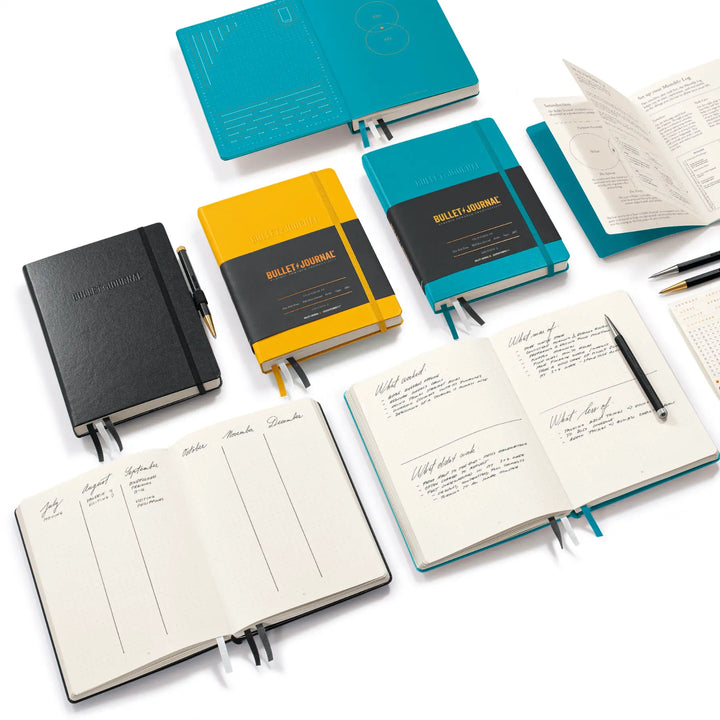Collection of bullet journal notebooks in various colors with open pages on a white background.
