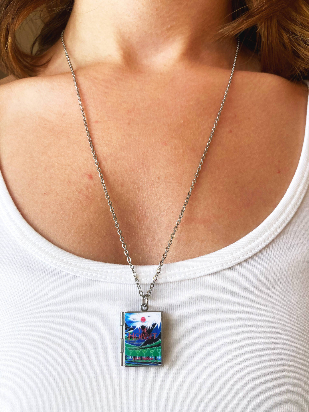 Necklace with a pendant featuring a scenic design worn by a person in a white tank top.