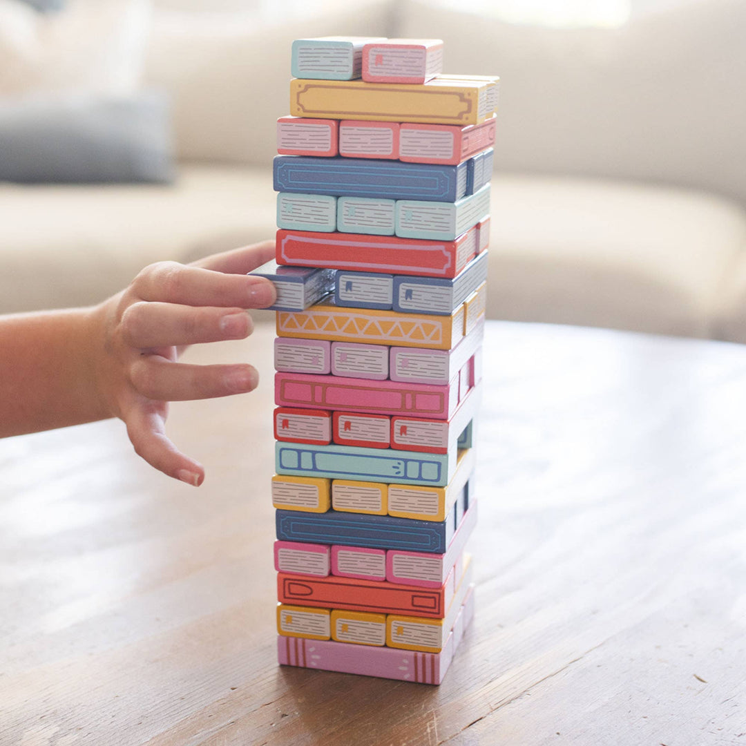 Pastel-colored card tower with a hand reaching to balance it on a light wooden surface.