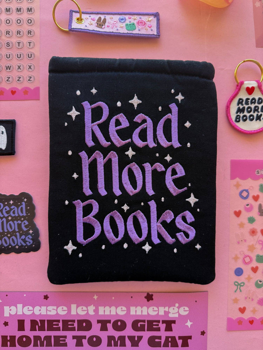 Black pouch with 'Read More Books' text on a pink background with decorative elements.