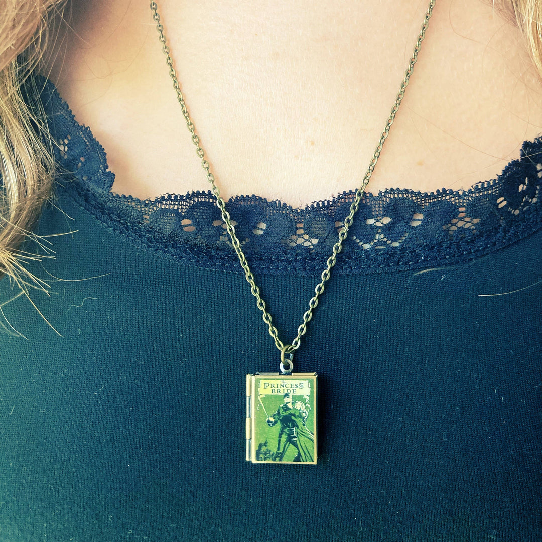 Necklace with a book-shaped pendant worn by a person in a blue top.