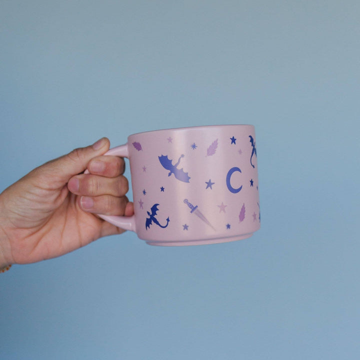 Hand holding a pink mug with fairy designs against a light blue background