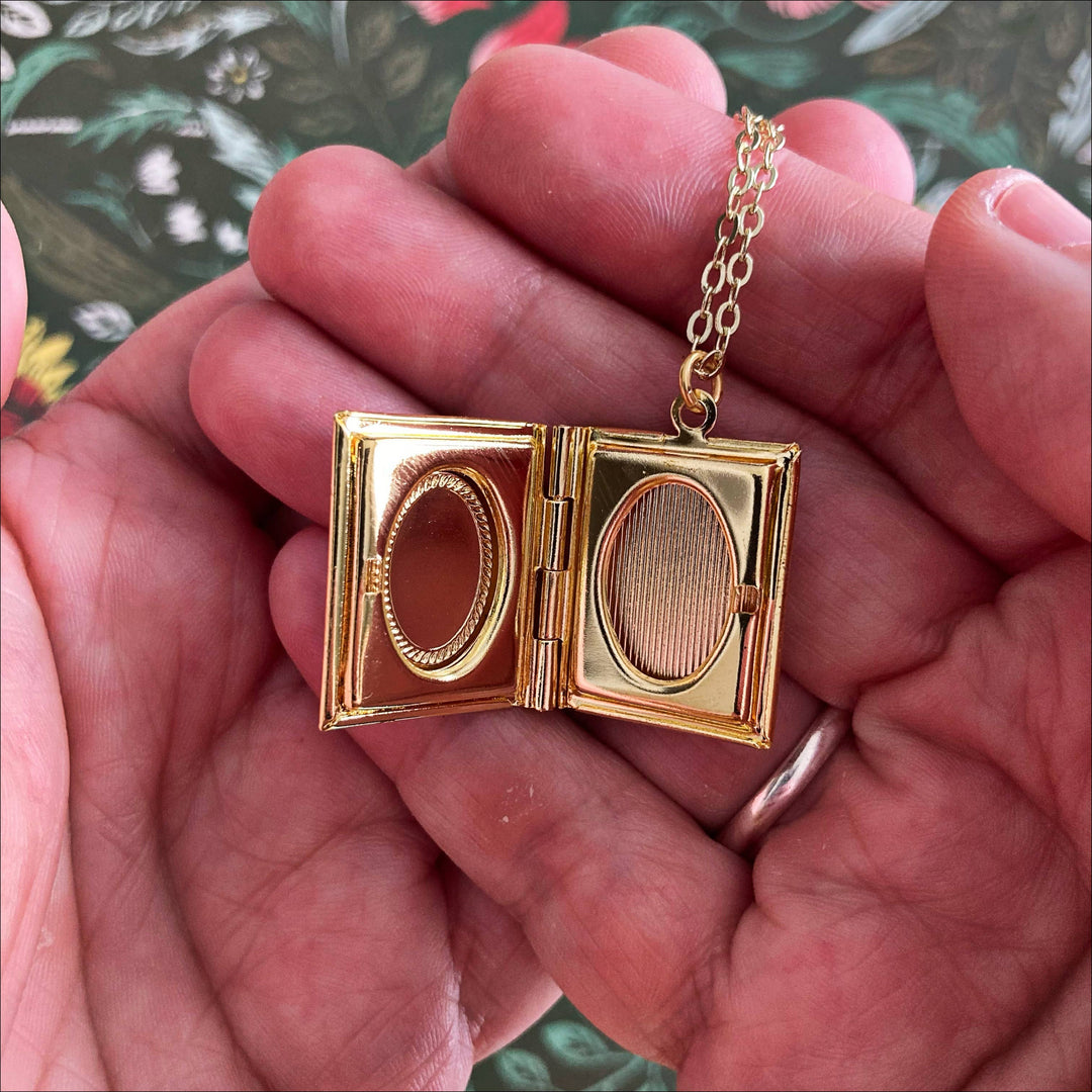 Gold locket with chain held in hands against a floral background