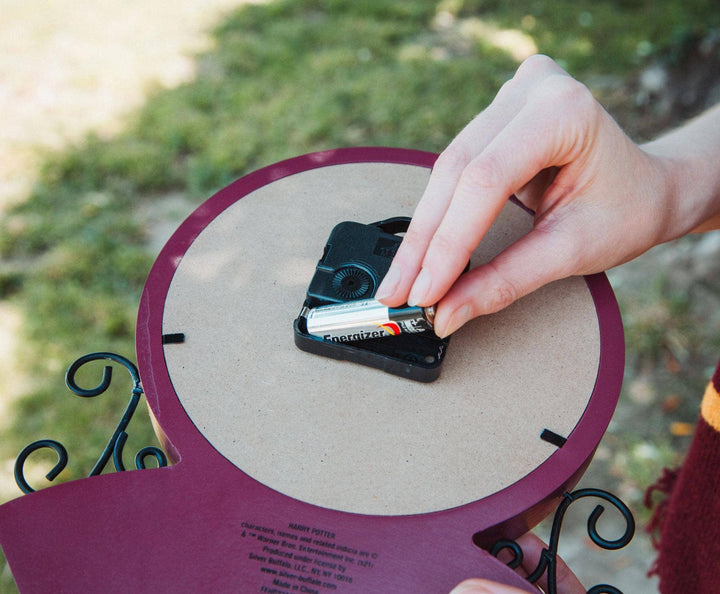 Person inserting batteries into a small black device on a round wooden board with purple rim.