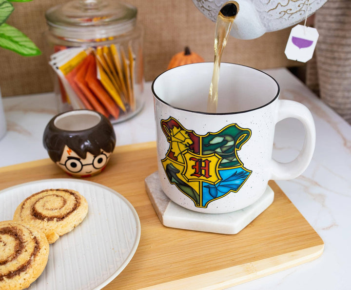 Tea being poured into a mug with a Hogwarts crest design on a wooden tray with cookies.