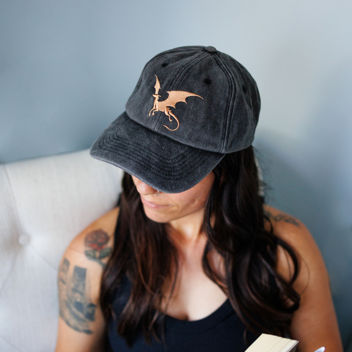 Person wearing a black cap with a dragon design against a gray background