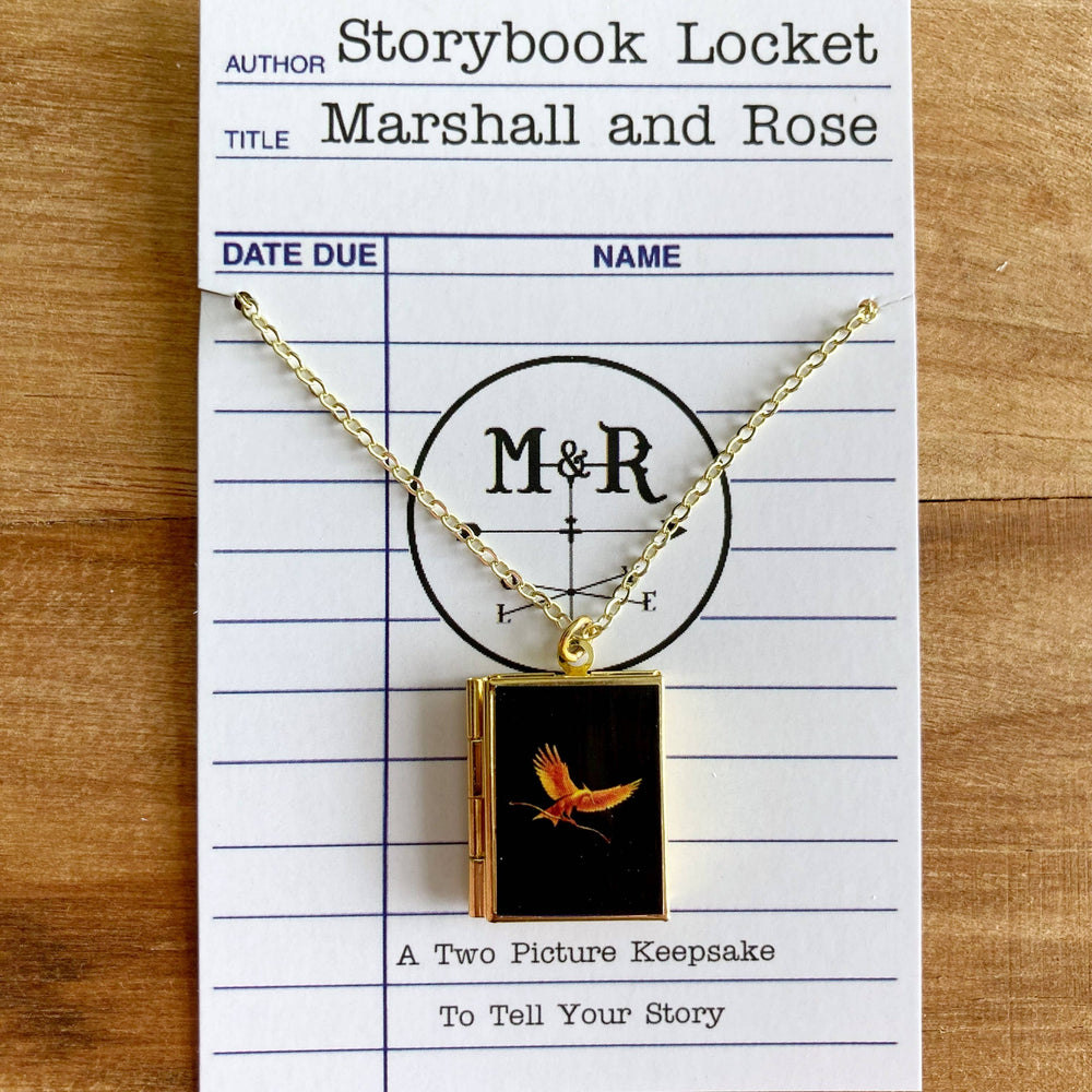 Gold necklace with a book-shaped pendant on a card labeled 'Storybook Locket' by Marshall and Rose.
