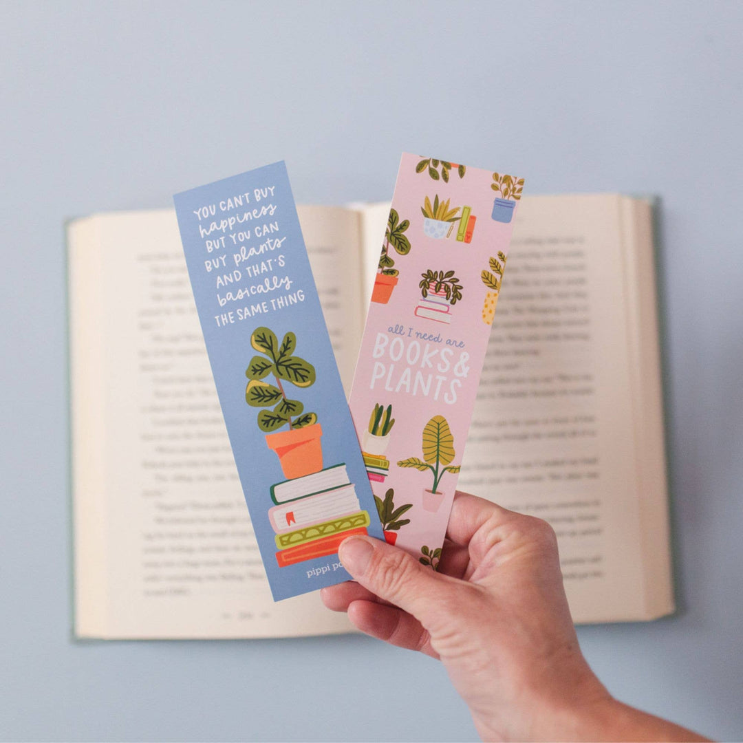 Hand holding two bookmarks with plant designs against an open book on a light blue background