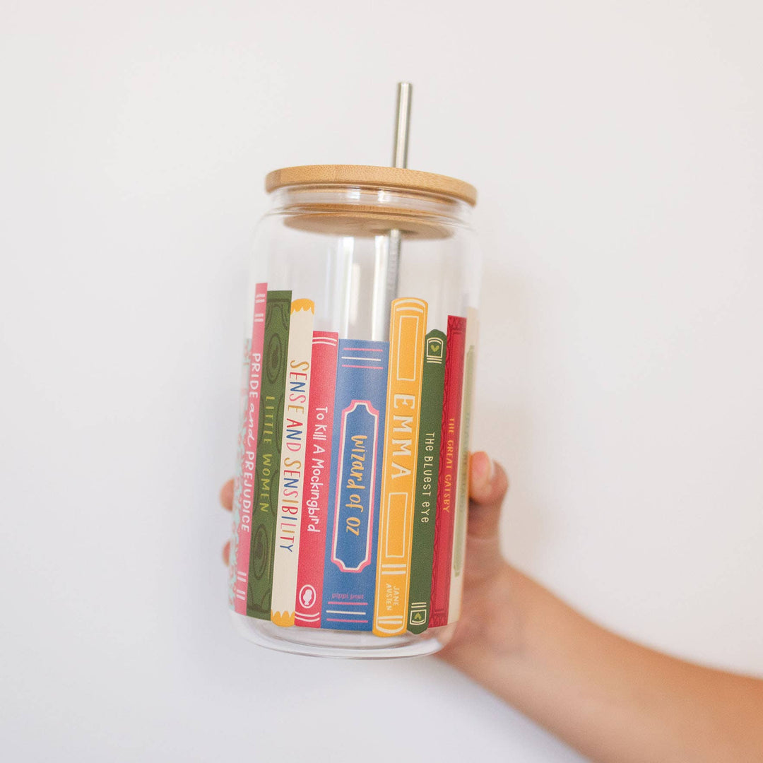 Glass tumbler with book-themed design held by a hand against a white background