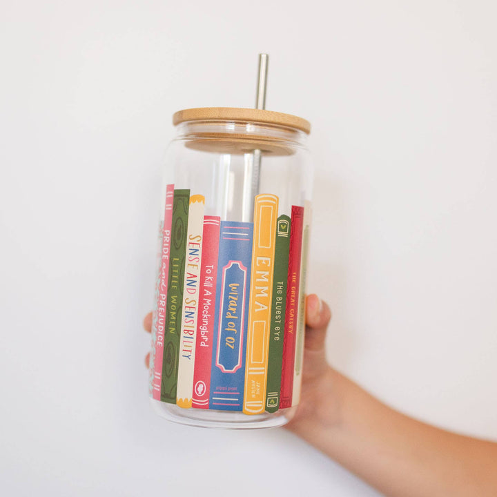 Glass tumbler with book-themed design held by a hand against a white background