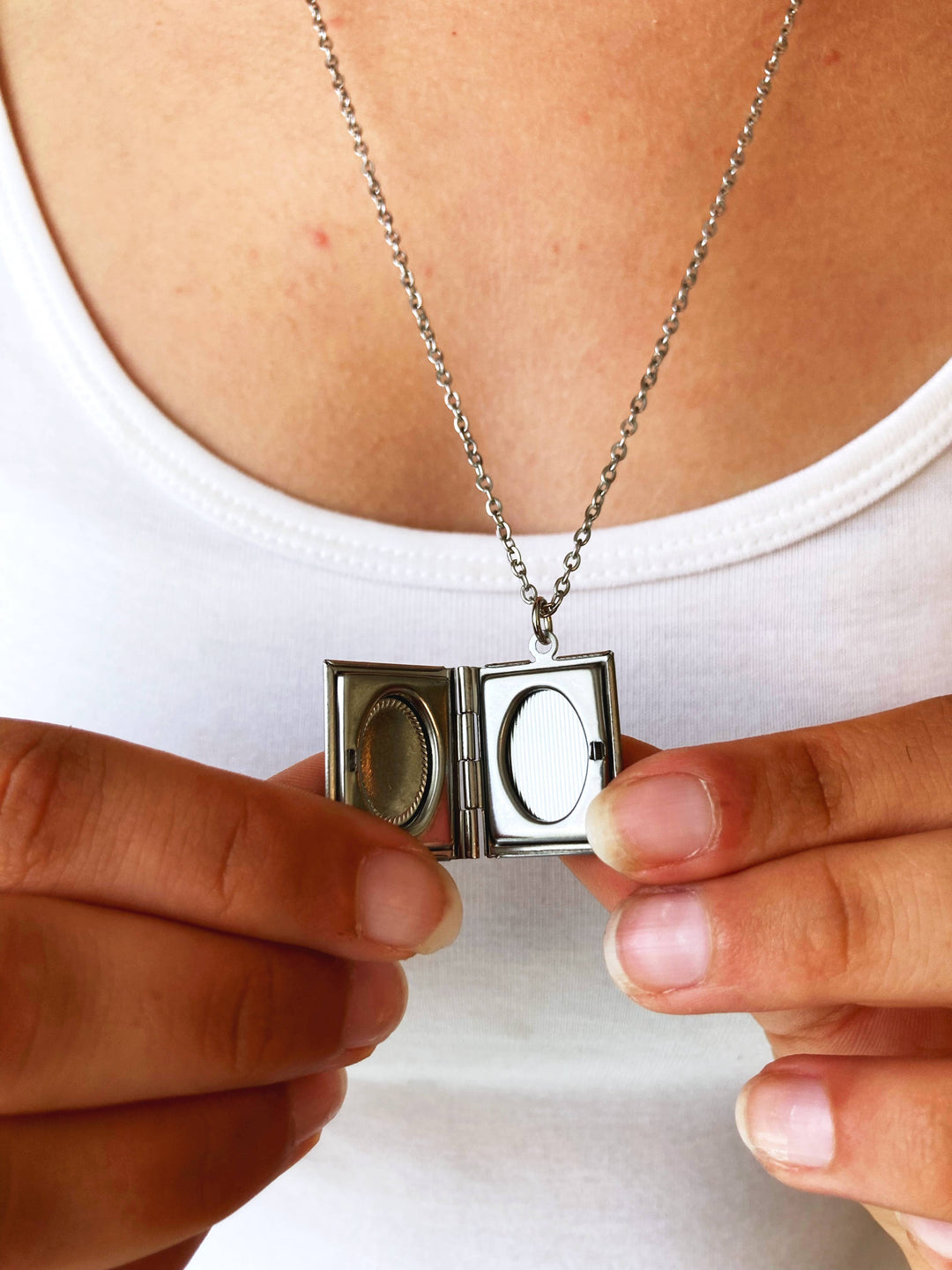 Person holding a silver locket with a chain against a white background