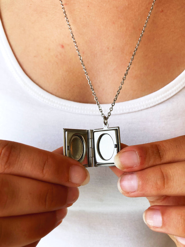 Person holding a silver locket with a chain against a white background
