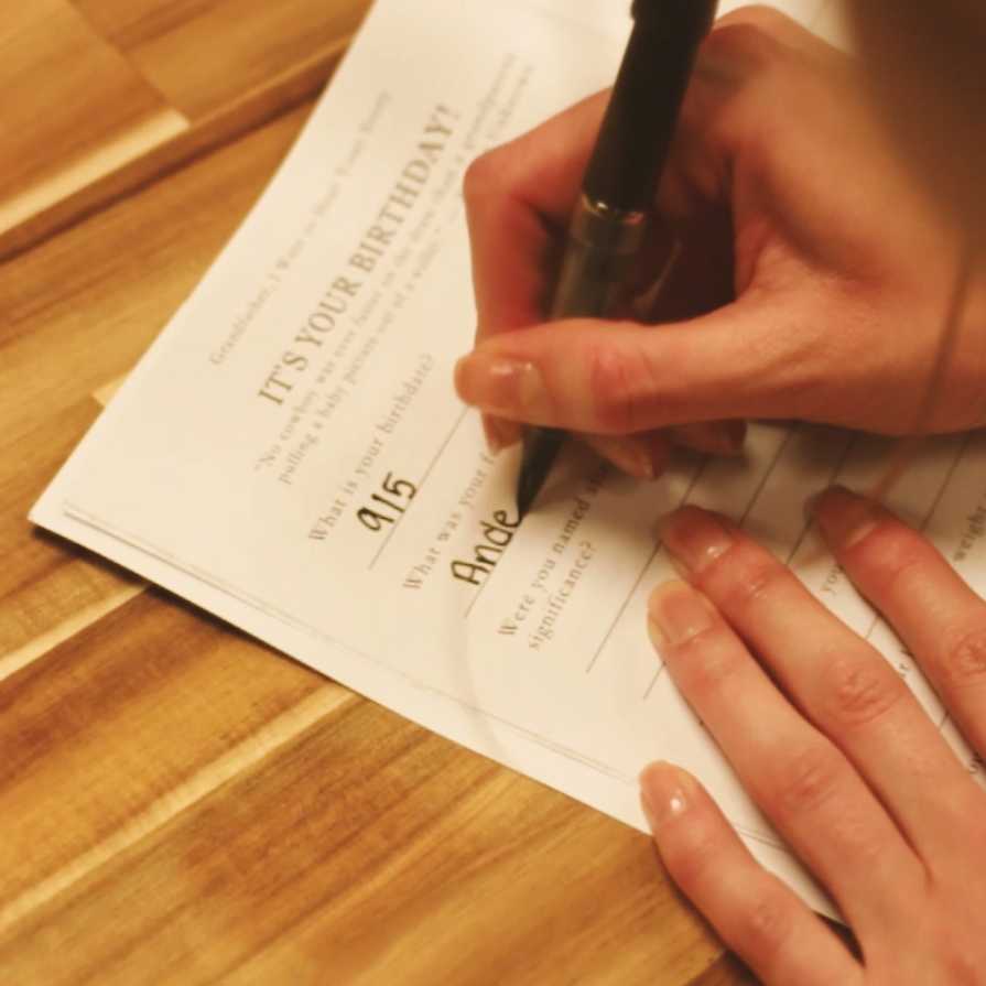 Hand writing on a birthday invitation with a pen on a wooden surface